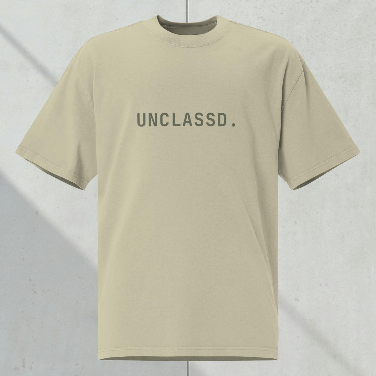 UNCLASSD CORE Oversized Tee in faded eucalyptus /sage with tonal “UNCLASSD.” chest print, ghost mockup against  concrete background.